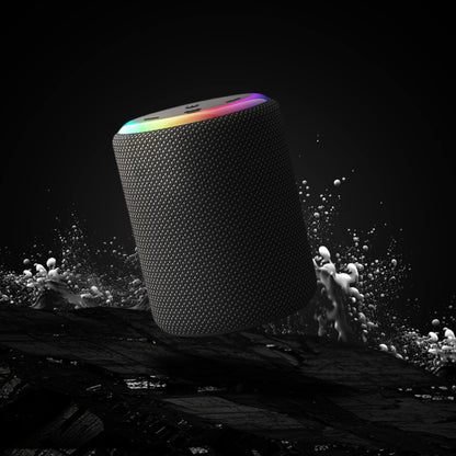 Photography of a cylindrical portable speaker with a dark gray mesh exterior and a vibrant RGB light ring on top, emerging from dynamic white water splashes against a dark background