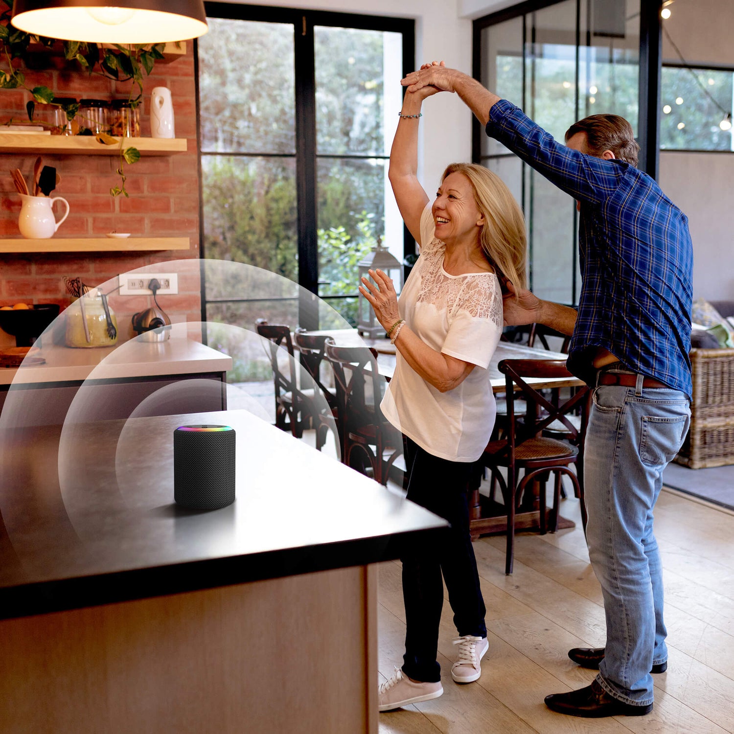 Dancing couple in a modern kitchen with a smart speaker featuring a colorful light ring on the counter, a brick wall backsplash, and large windows