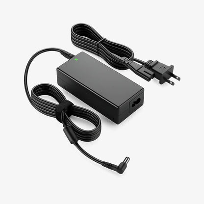 Digital photograph of a black laptop power adapter on a white background featuring a rectangular power brick with a green LED indicator light, a coiled power cable with a two-prong US plug, and a coiled output cable with a right-angle DC tip.