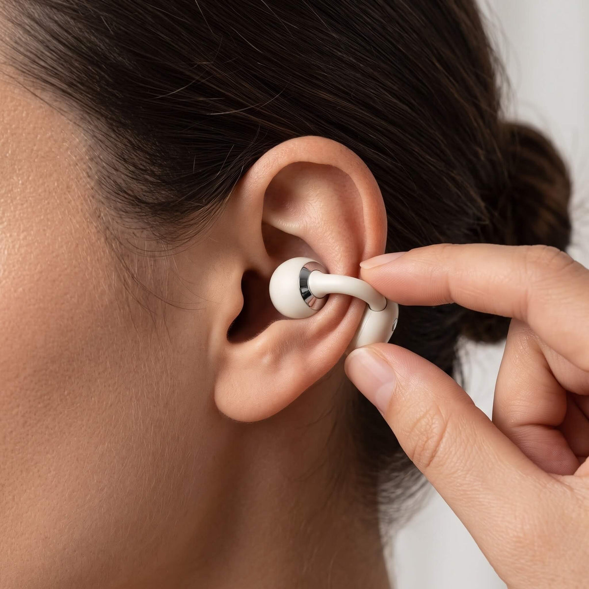 A hand clipping an ivory ViSound Ease onto the outer edge of an ear